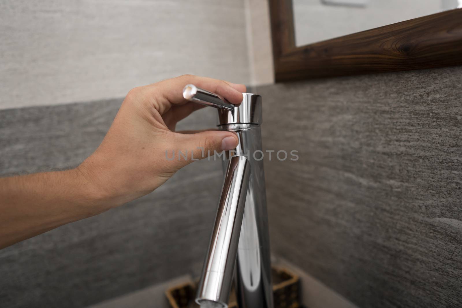 Male hand use a faucet in a bathroom interior with white round sink and chrome faucet. Water flowing from the chrome faucet