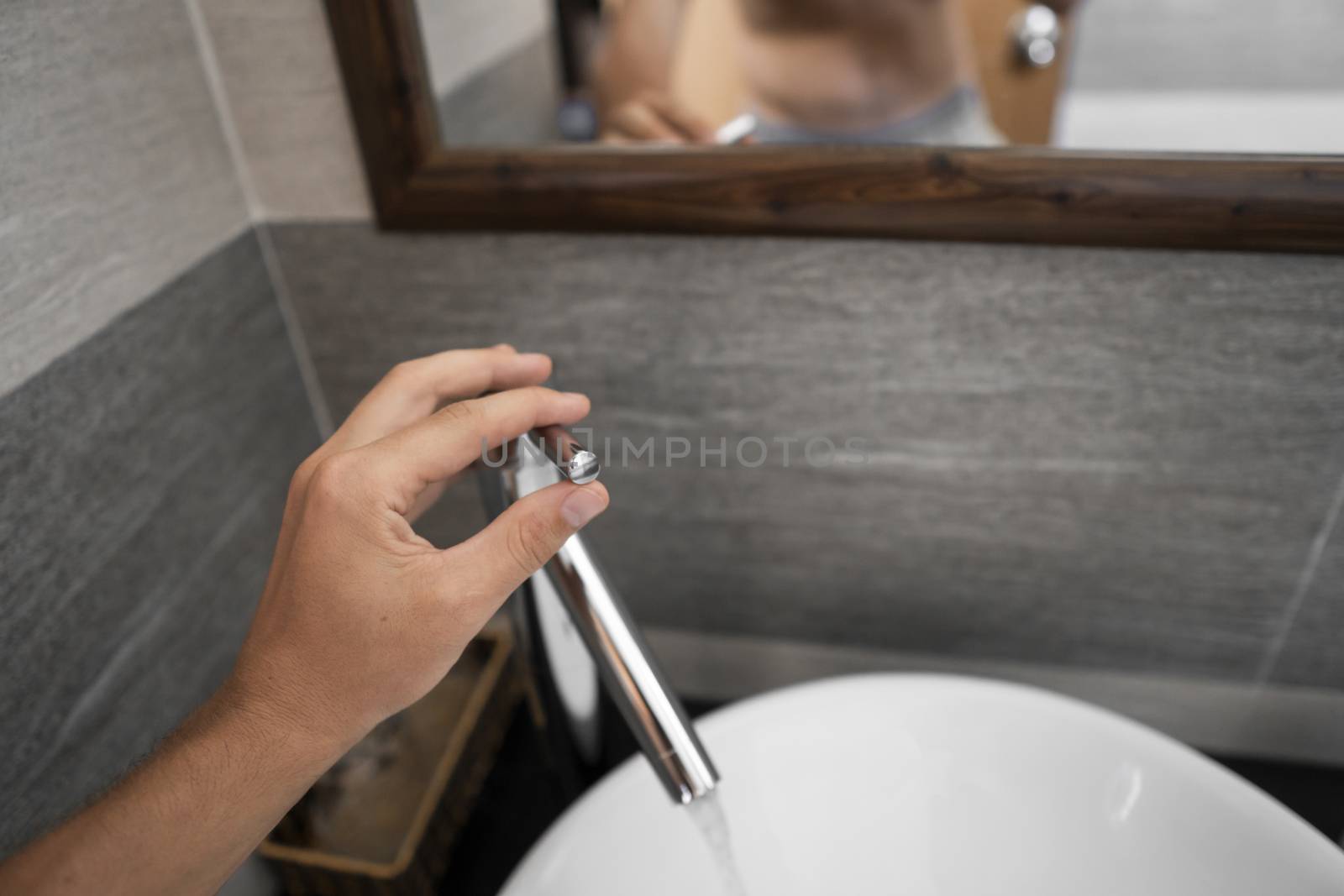 Male hand use a faucet in a bathroom interior with white round sink and chrome faucet. Water flowing from the chrome faucet. by vovsht