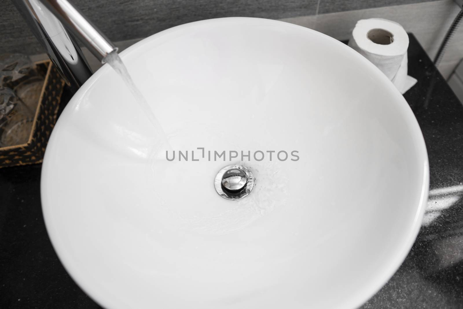 Bathroom interior with white round sink and chrome faucet in a modern bathroom. Water flowing from the chrome faucet