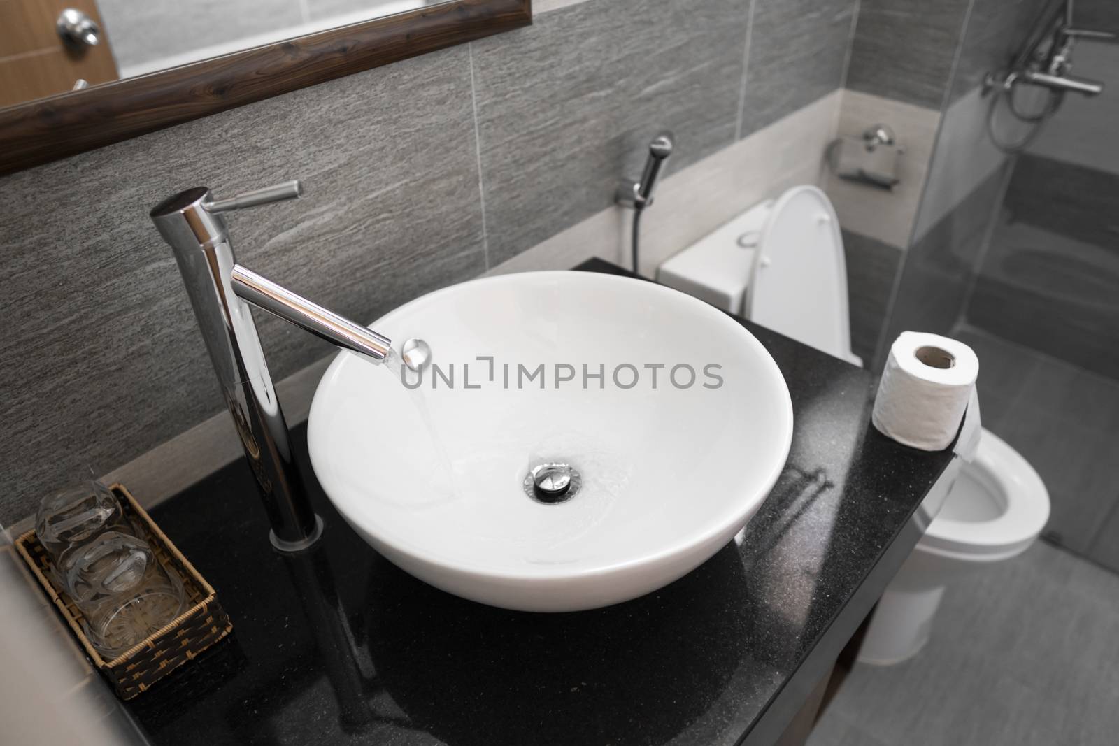 Bathroom interior with white round sink and chrome faucet in a modern bathroom. Water flowing from the chrome faucet