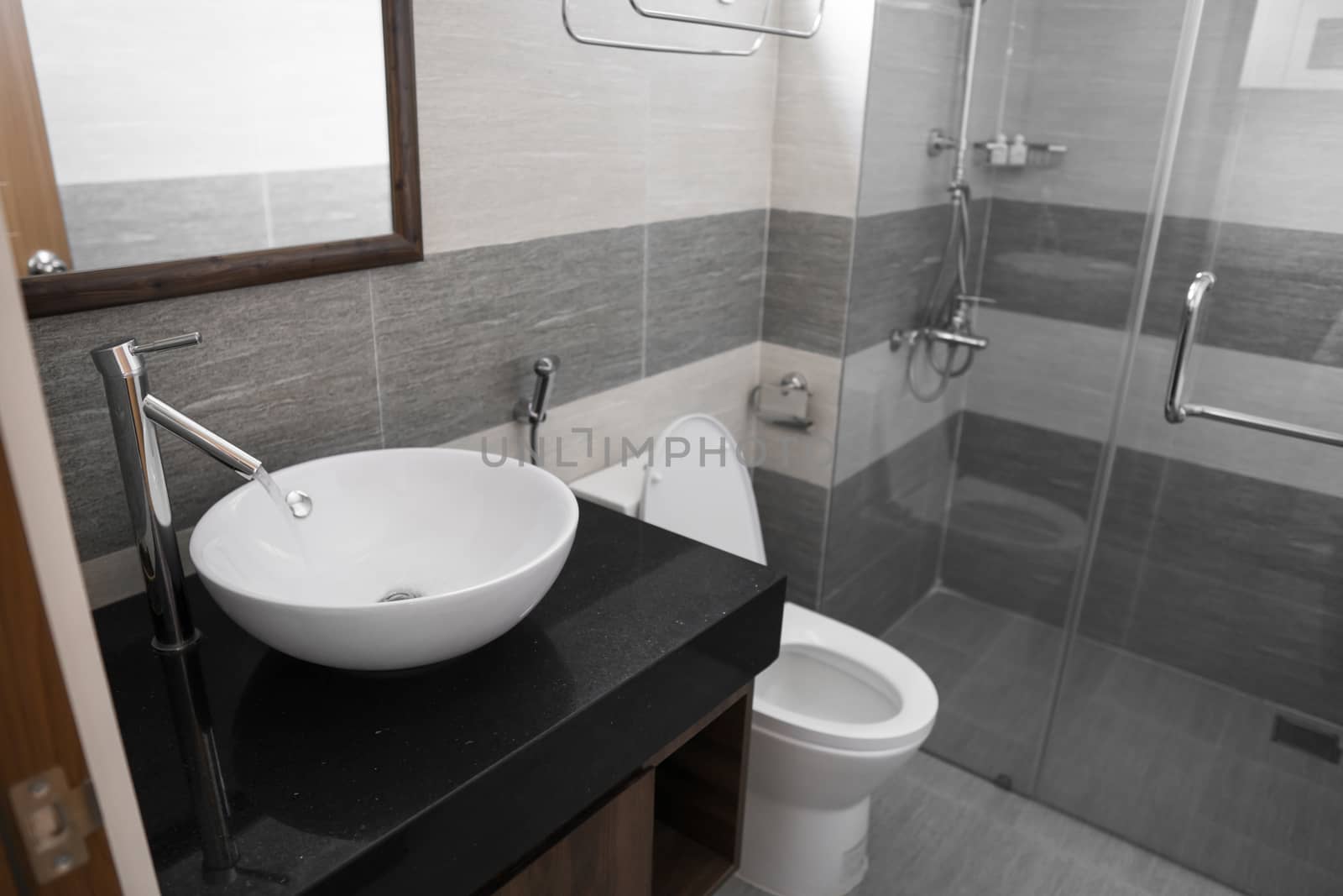 Bathroom interior with white round sink and chrome faucet in a modern bathroom with a toilet and shower. Water flowing from the chrome faucet