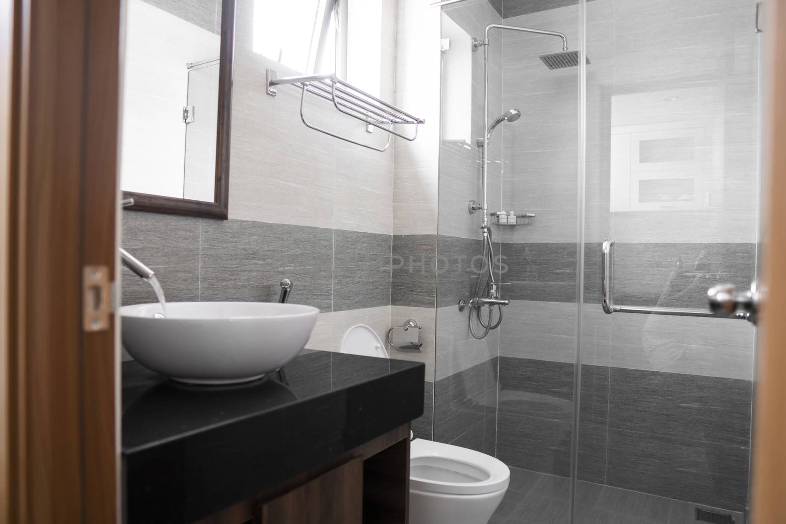 Bathroom interior with white round sink and chrome faucet in a modern bathroom with a toilet and shower. Water flowing from the chrome faucet