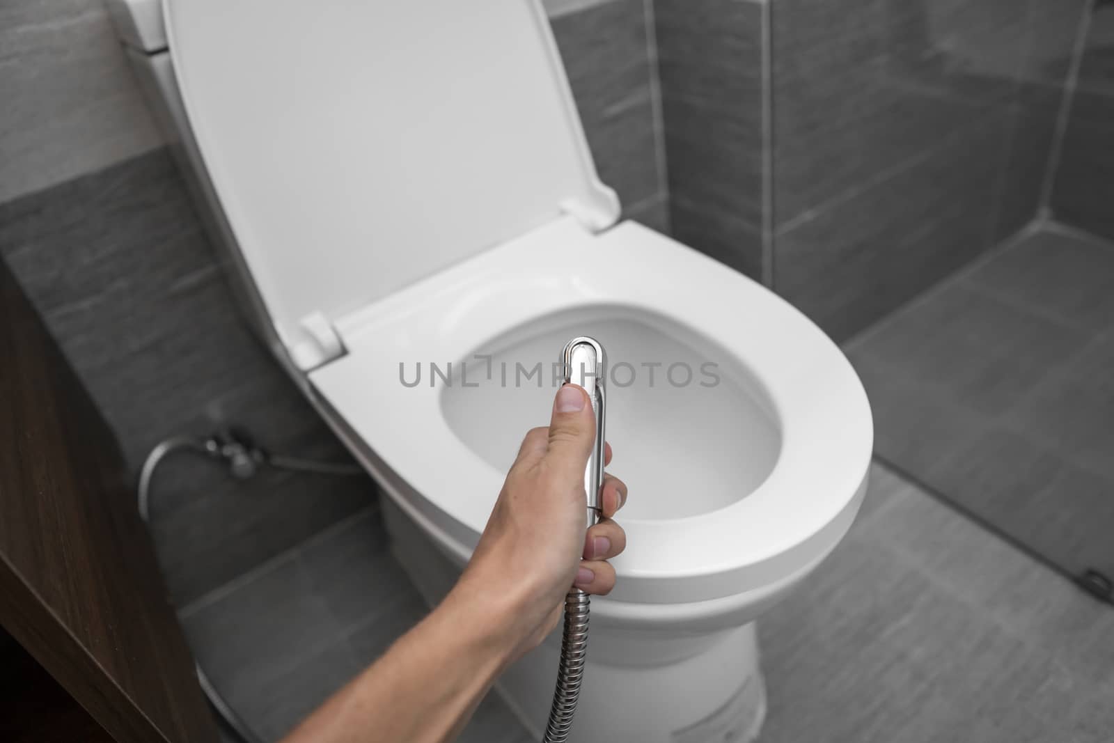 Using of bidet shower with a white toilet. Bidet shower in male hand for using with a white toilet bowl. by vovsht