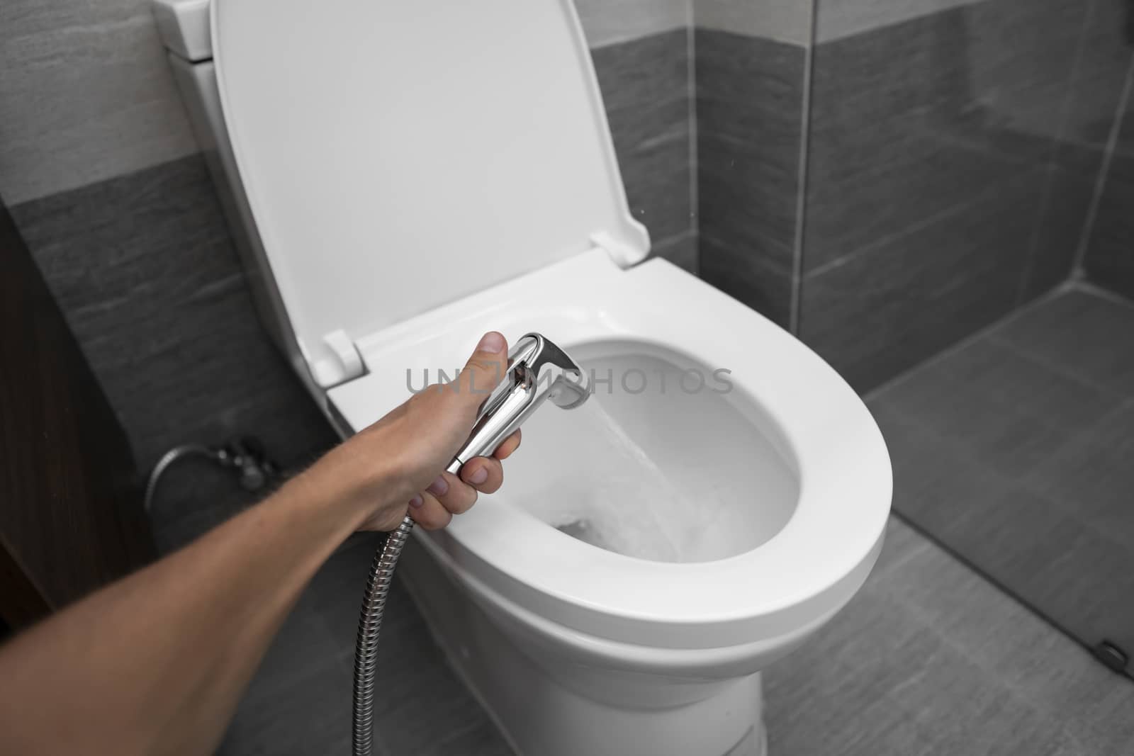 Using of bidet shower with a white toilet. Bidet shower in male hand for using with a white toilet bowl. by vovsht