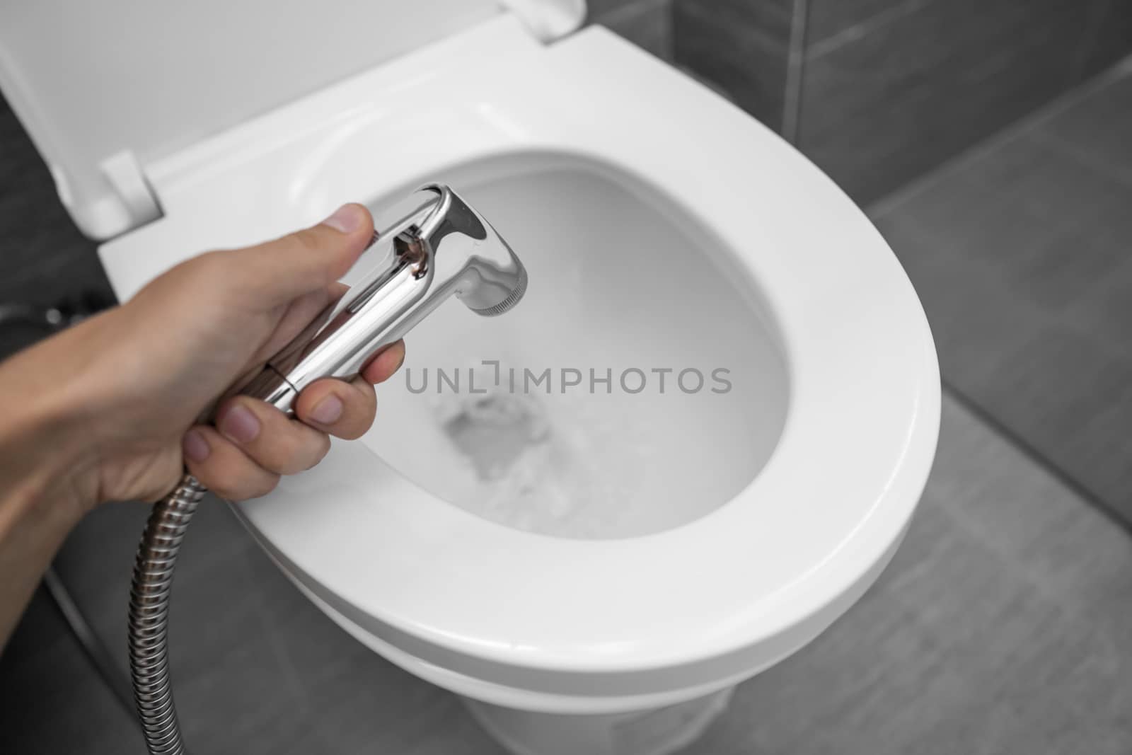 Using of bidet shower with a white toilet. Bidet shower in male hand for using with a white toilet bowl. by vovsht