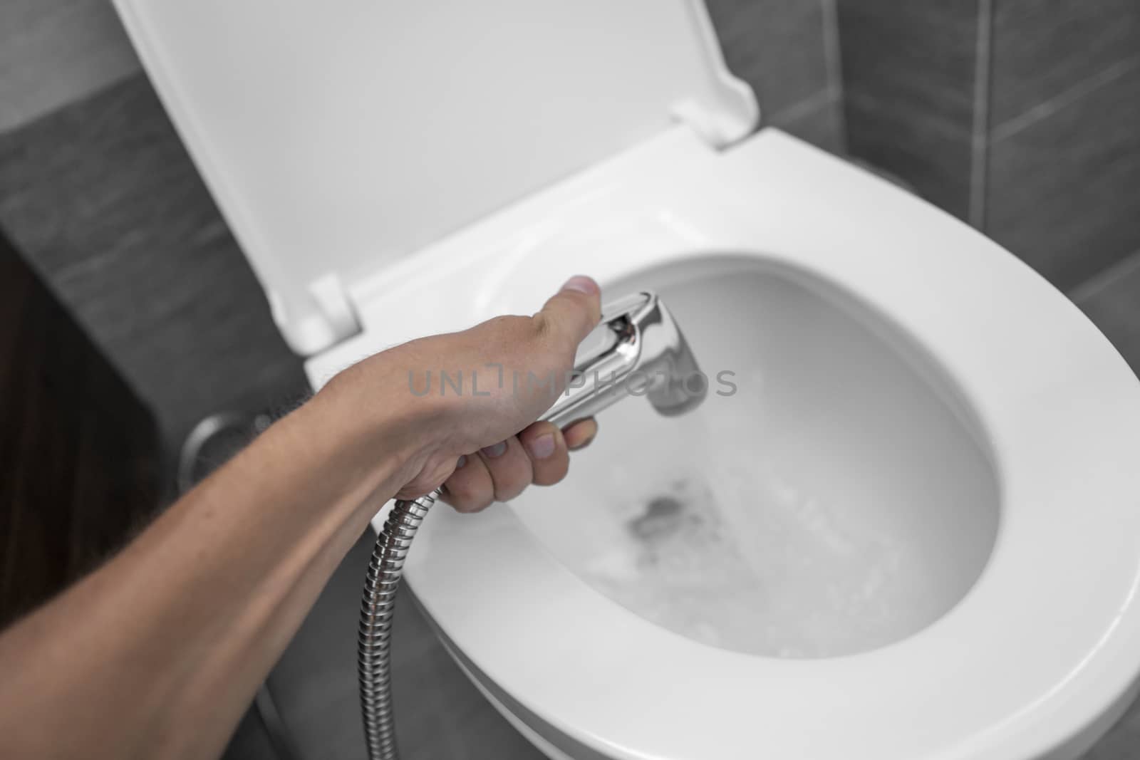 Using of bidet shower with a white toilet. Bidet shower in male hand for using with a white toilet bowl