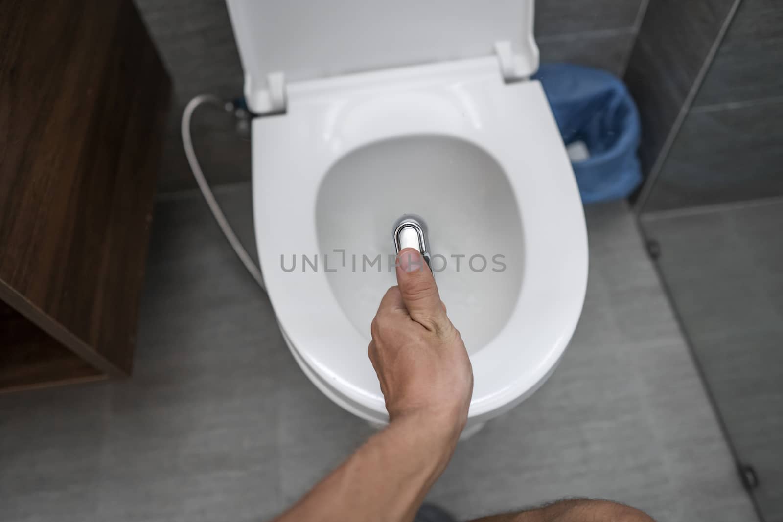 Using of bidet shower with a white toilet. Bidet shower in male hand for using with a white toilet bowl