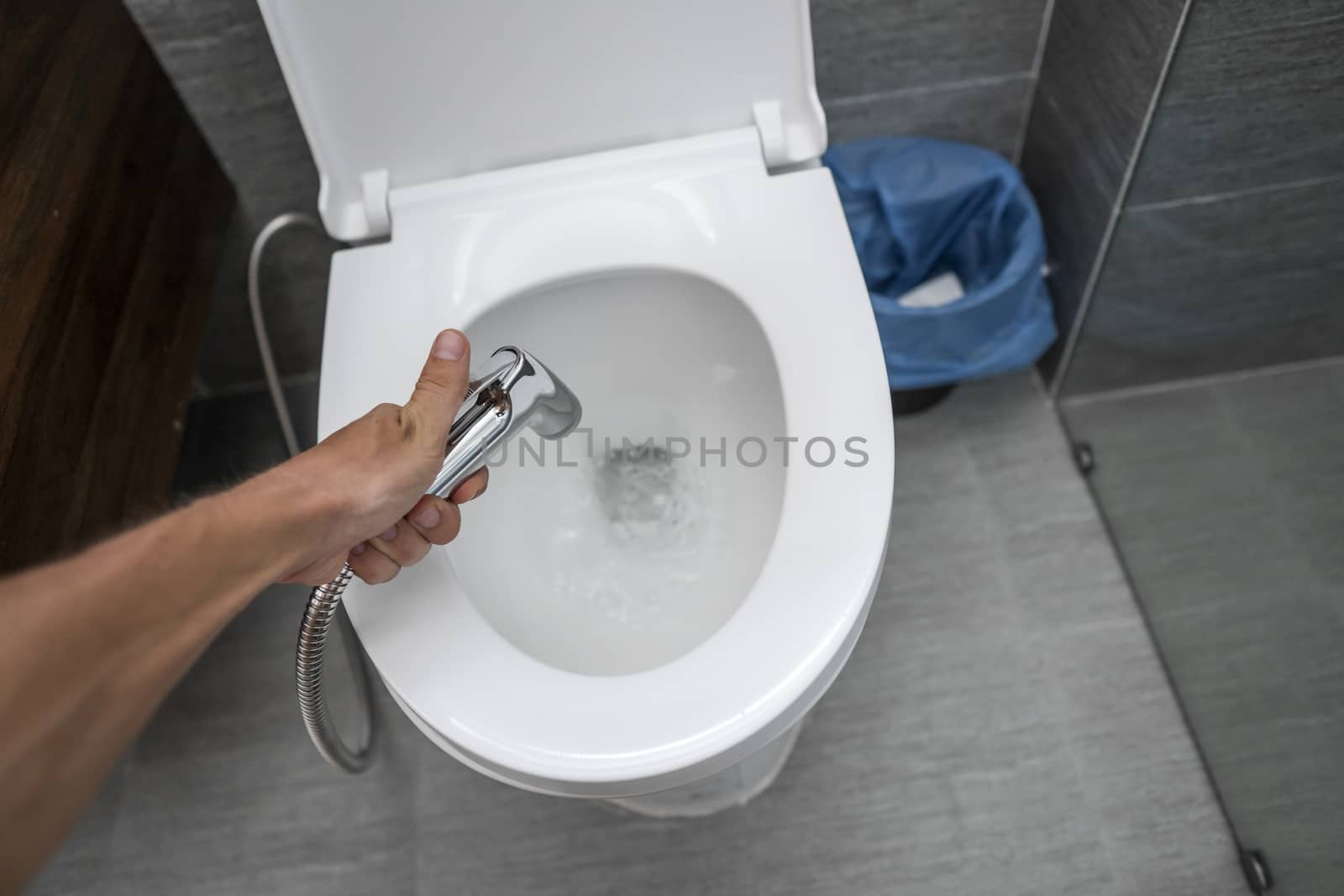 Using of bidet shower with a white toilet. Bidet shower in male hand for using with a white toilet bowl. by vovsht