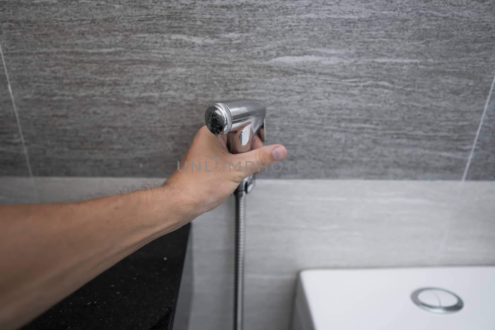 Using of bidet shower in bathroom with a bidet or toiler. Bidet shower in male hand for using it in a bathroom