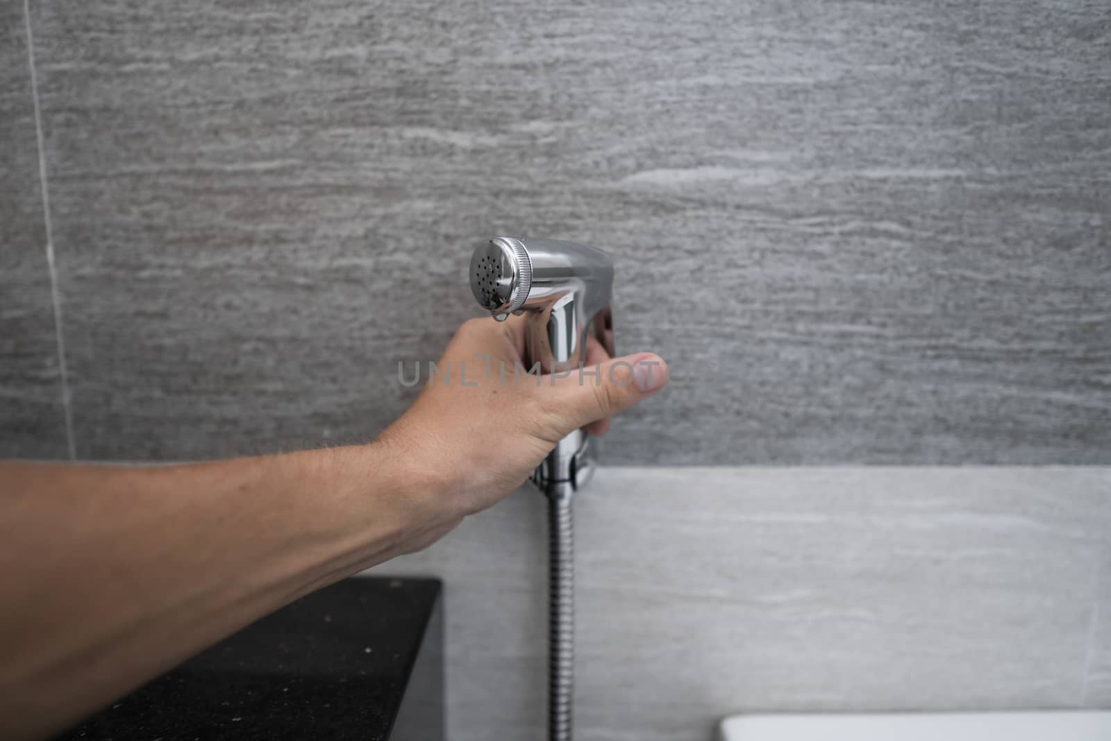 Using of bidet shower in bathroom with a bidet or toiler. Bidet shower in male hand for using it in a bathroom