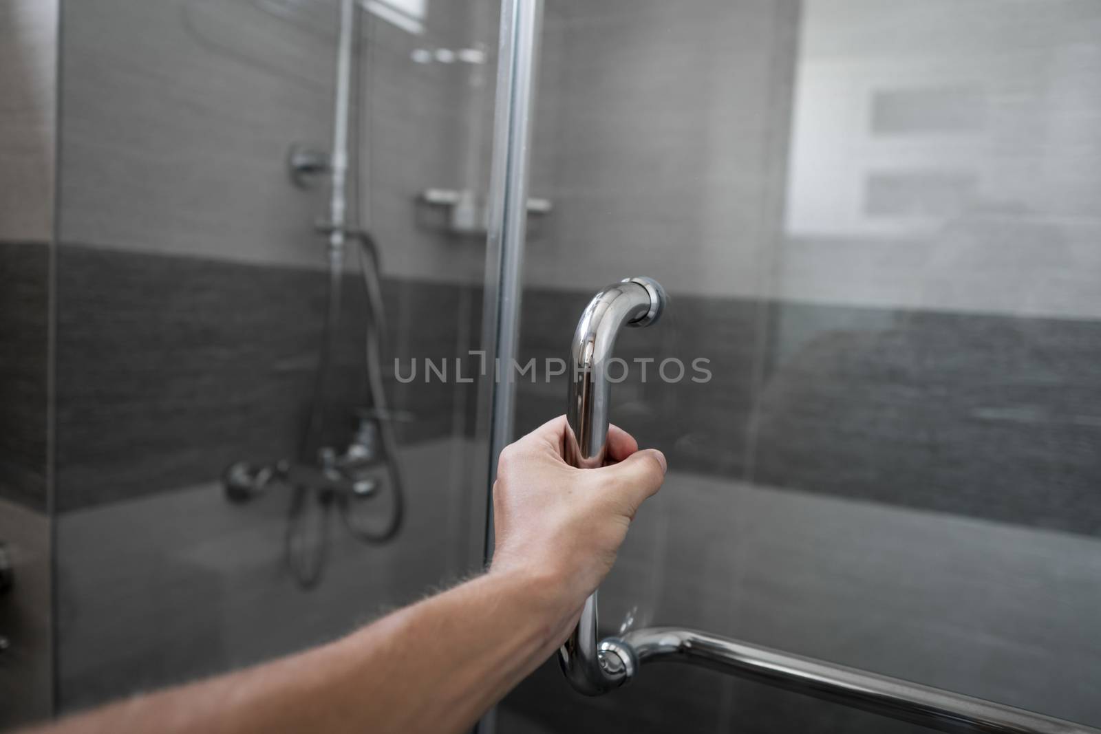 Male hand opens the shower door in a modern bathroom