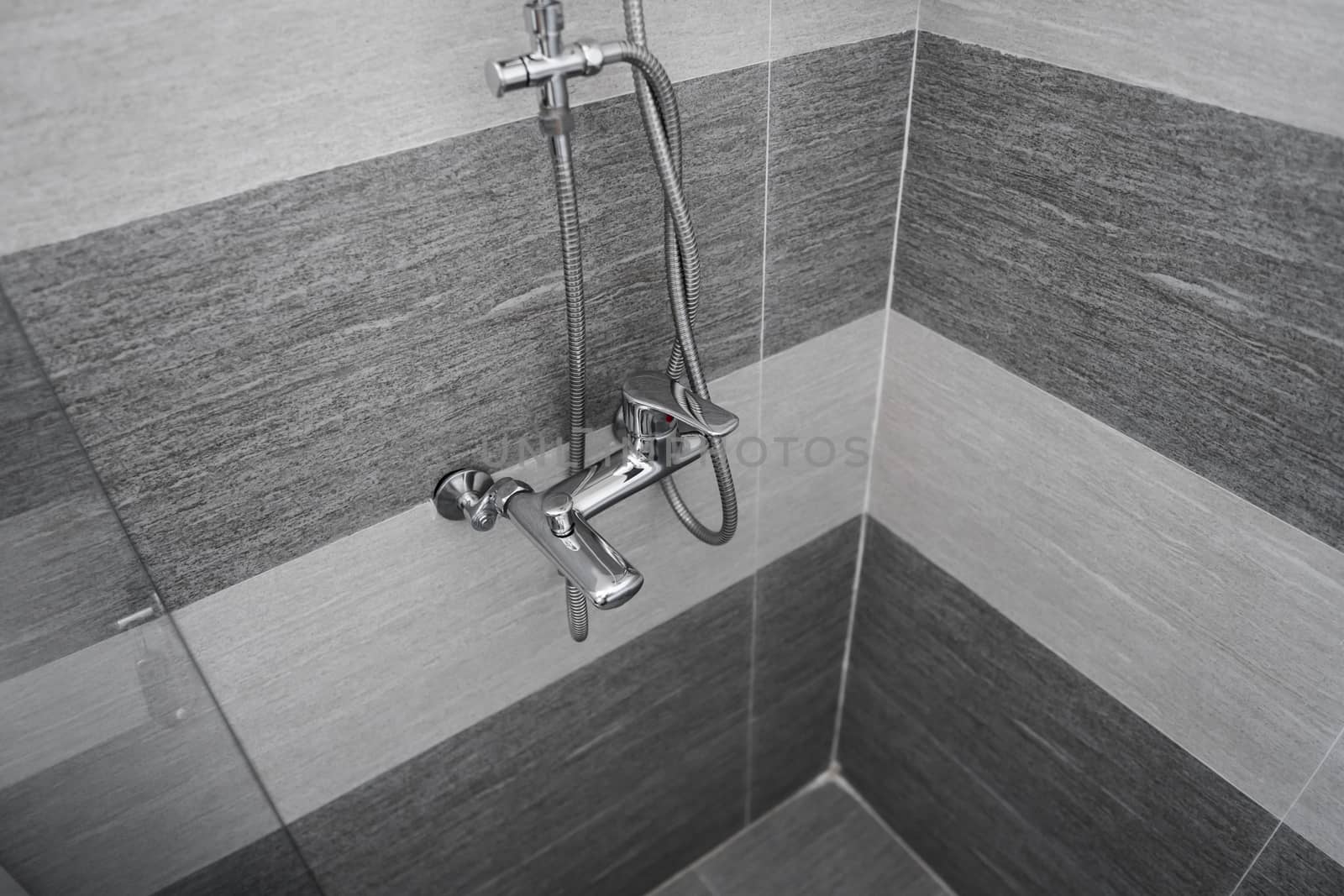Modern designer tap and shower in bathroom. Closeup of chrome shower, faucet, in the bathroom covered decorative ceramic. Mixer cold hot water
