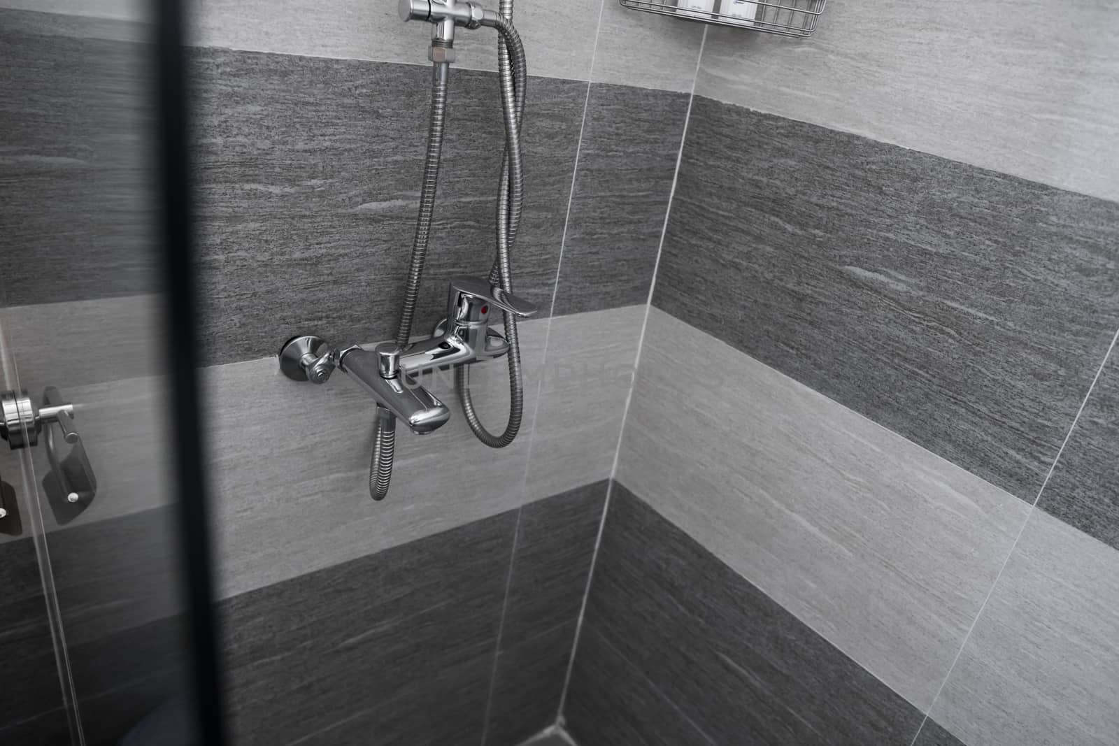 Modern designer tap and shower in bathroom. Closeup of chrome shower, faucet, in the bathroom covered decorative ceramic. Mixer cold hot water