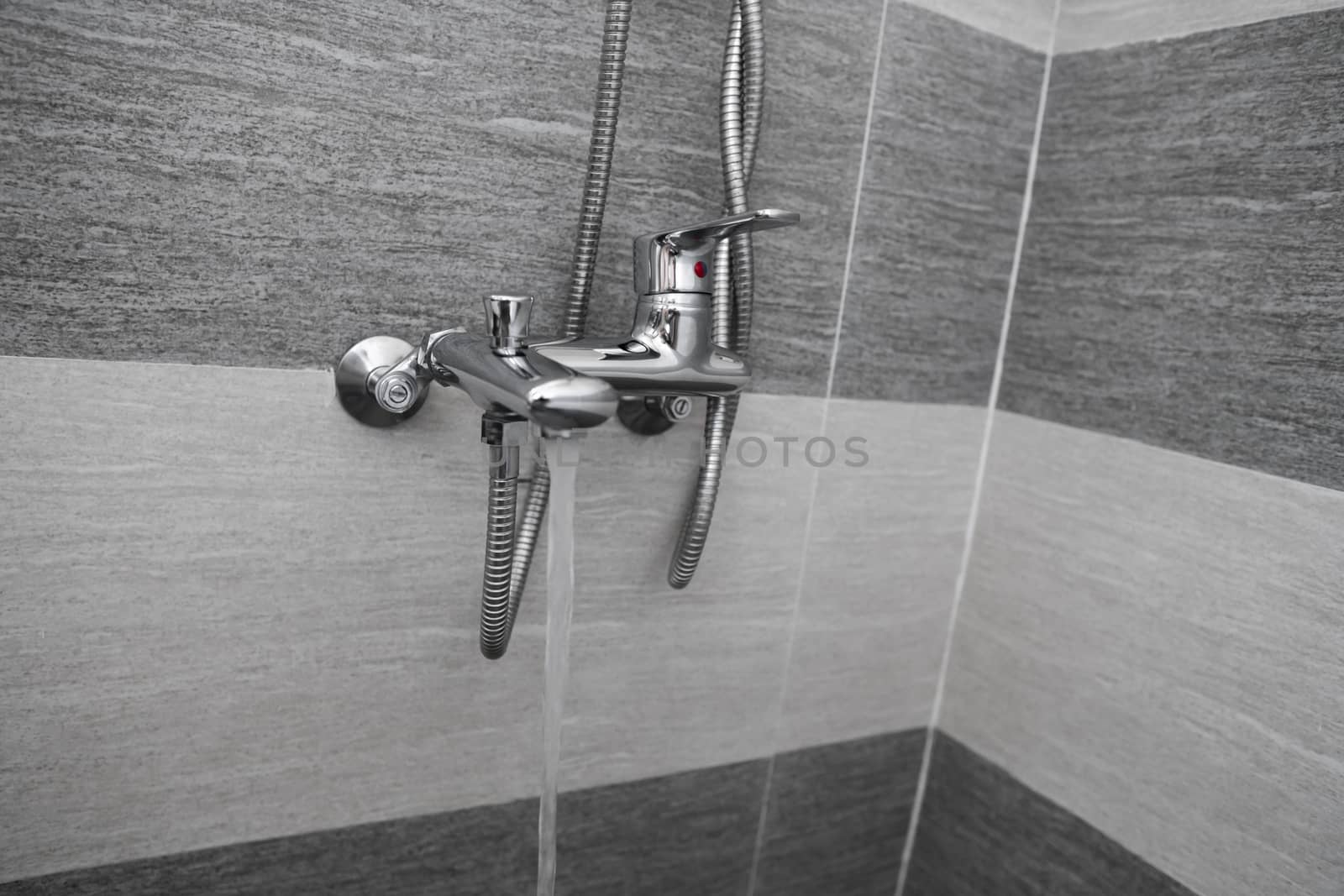 Water flows from the mixer. Modern designer tap and shower in bathroom. Closeup of chrome shower, faucet, in the bathroom covered decorative ceramic. Mixer cold hot water