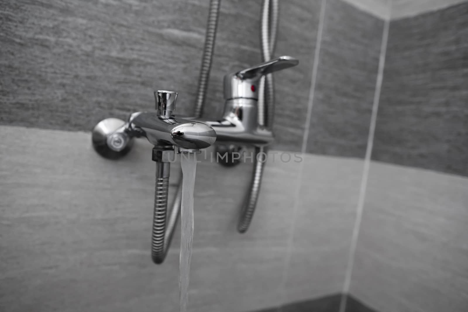 Water flows from the mixer. Modern designer tap and shower in bathroom. Closeup of chrome shower, faucet, in the bathroom covered decorative ceramic. Mixer cold hot water
