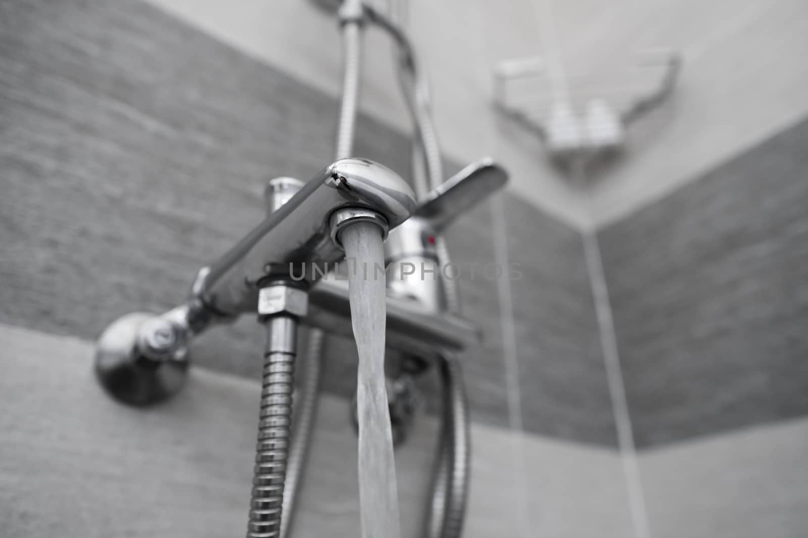 Water flows from the mixer. Modern designer tap and shower in bathroom. Closeup of chrome shower, faucet, in the bathroom covered decorative ceramic. Mixer cold hot water