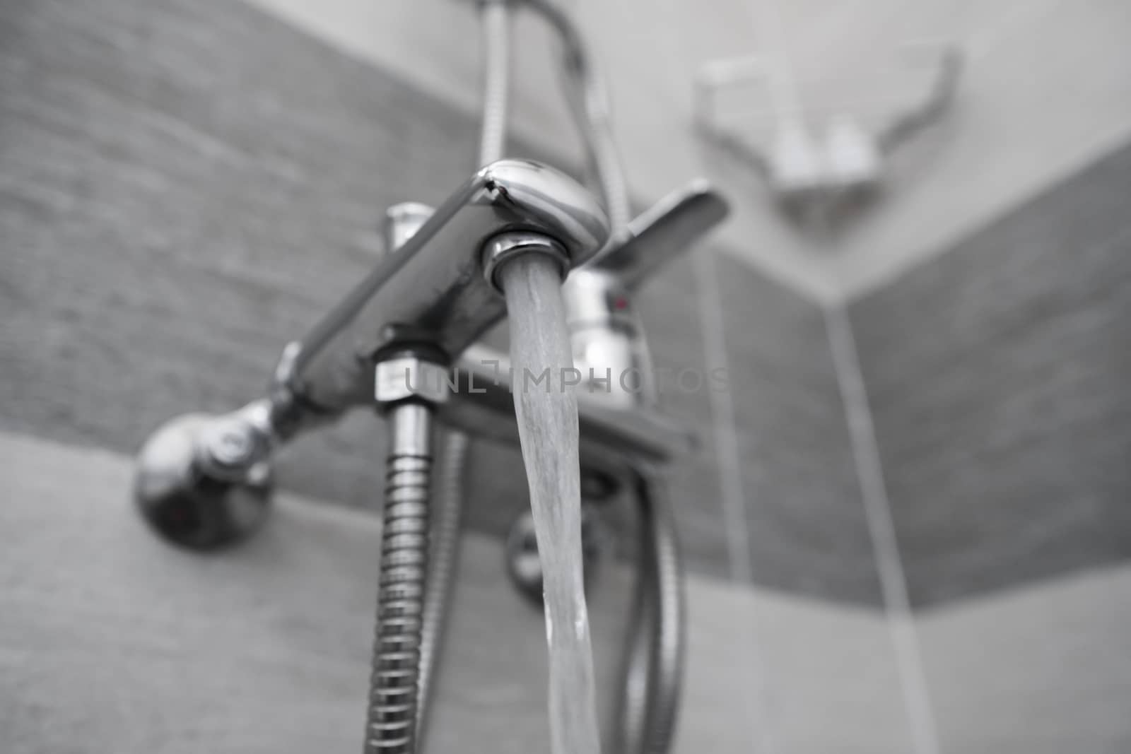 Water flows from the mixer. Modern designer tap and shower in bathroom. Closeup of chrome shower, faucet, in the bathroom covered decorative ceramic. Mixer cold hot water
