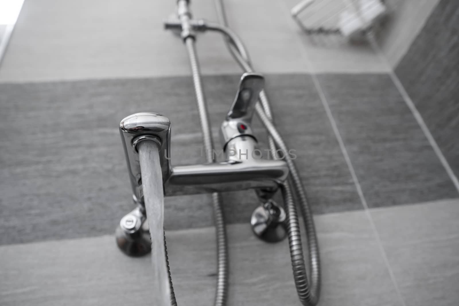 Water flows from the mixer. Modern designer tap and shower in bathroom. Closeup of chrome shower, faucet, in the bathroom covered decorative ceramic. Mixer cold hot water