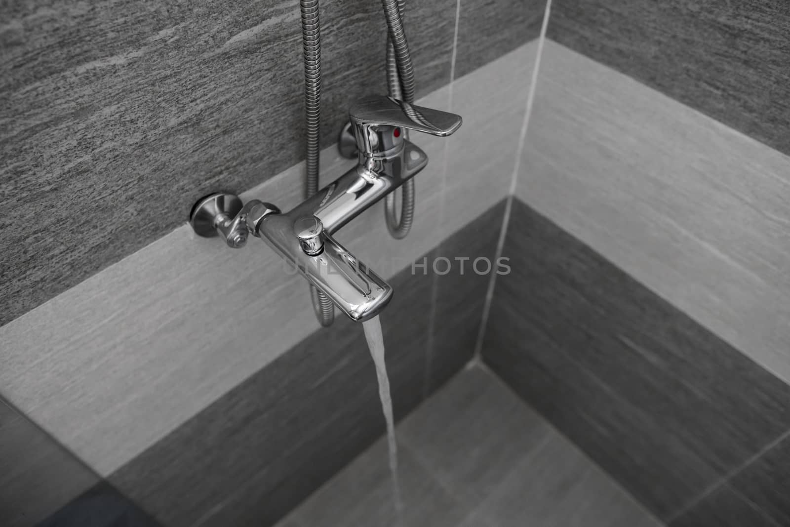 Water flows from the mixer. Modern designer tap and shower in bathroom. Closeup of chrome shower, faucet, in the bathroom covered decorative ceramic. Mixer cold hot water