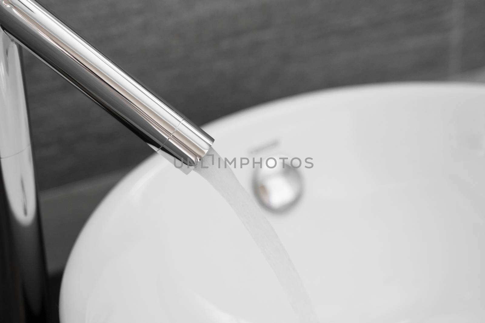 Bathroom interior with white round sink and chrome faucet in a modern bathroom. Water flowing from the chrome faucet