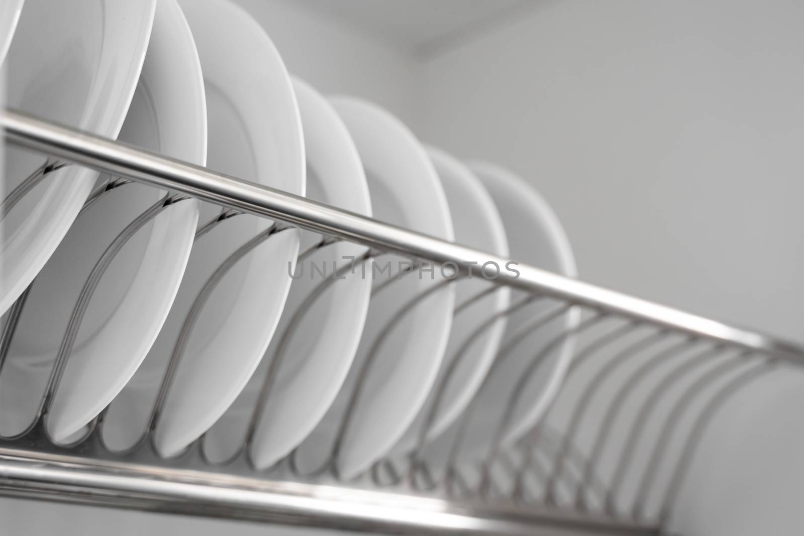 Dish drying metal rack with big nice white clean plates. Traditional comfortable kitchen. Open white dish draining closet with wet dishes of glass and ceramic, plates, bowls drying inside on rack. by vovsht