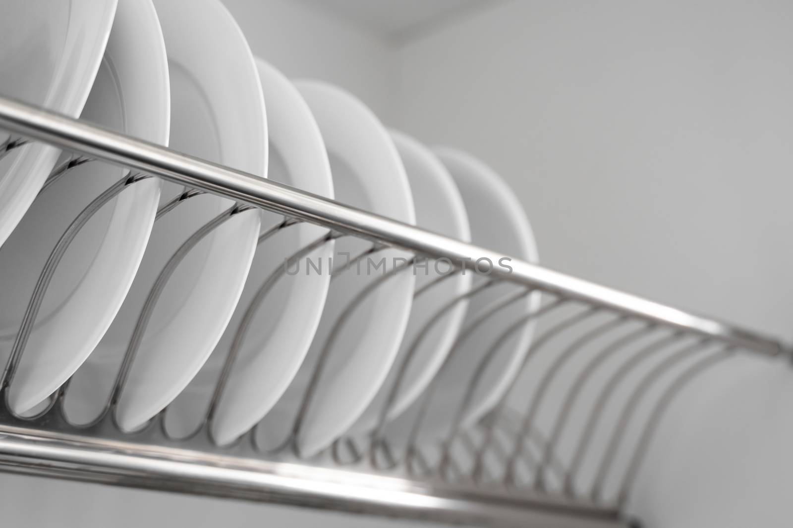 Dish drying metal rack with big nice white clean plates. Traditional comfortable kitchen. Open white dish draining closet with wet dishes of glass and ceramic, plates, bowls drying inside on rack