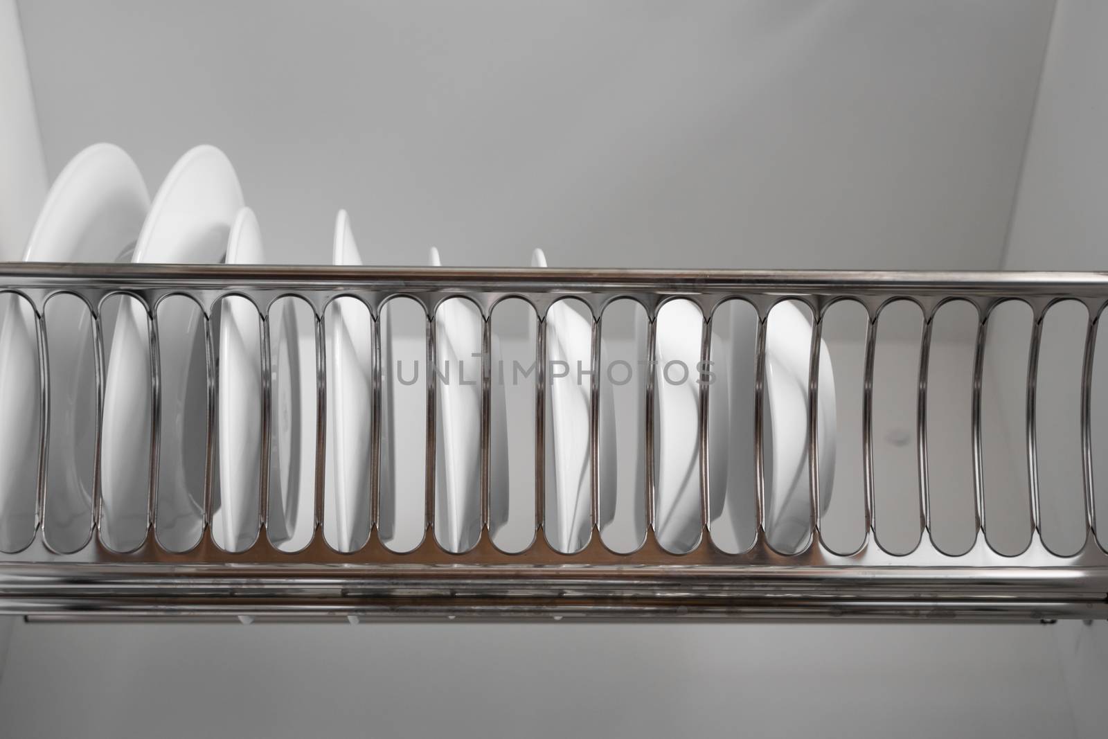 Dish drying metal rack with big nice white clean plates. Traditional comfortable kitchen. Open white dish draining closet with wet dishes of glass and ceramic, plates, bowls drying inside on rack