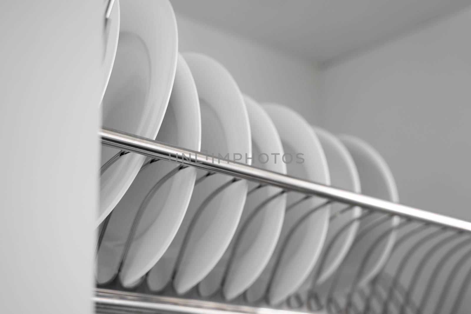 Dish drying metal rack with big nice white clean plates. Traditional comfortable kitchen. Open white dish draining closet with wet dishes of glass and ceramic, plates, bowls drying inside on rack