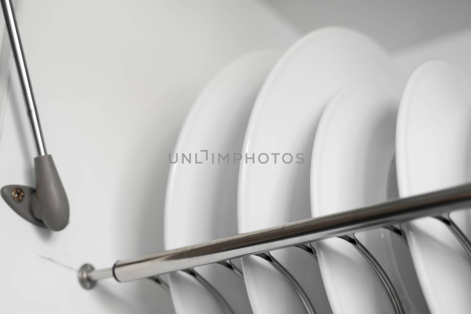 Dish drying metal rack with big nice white clean plates. Traditional comfortable kitchen. Open white dish draining closet with wet dishes of glass and ceramic, plates, bowls drying inside on rack. by vovsht