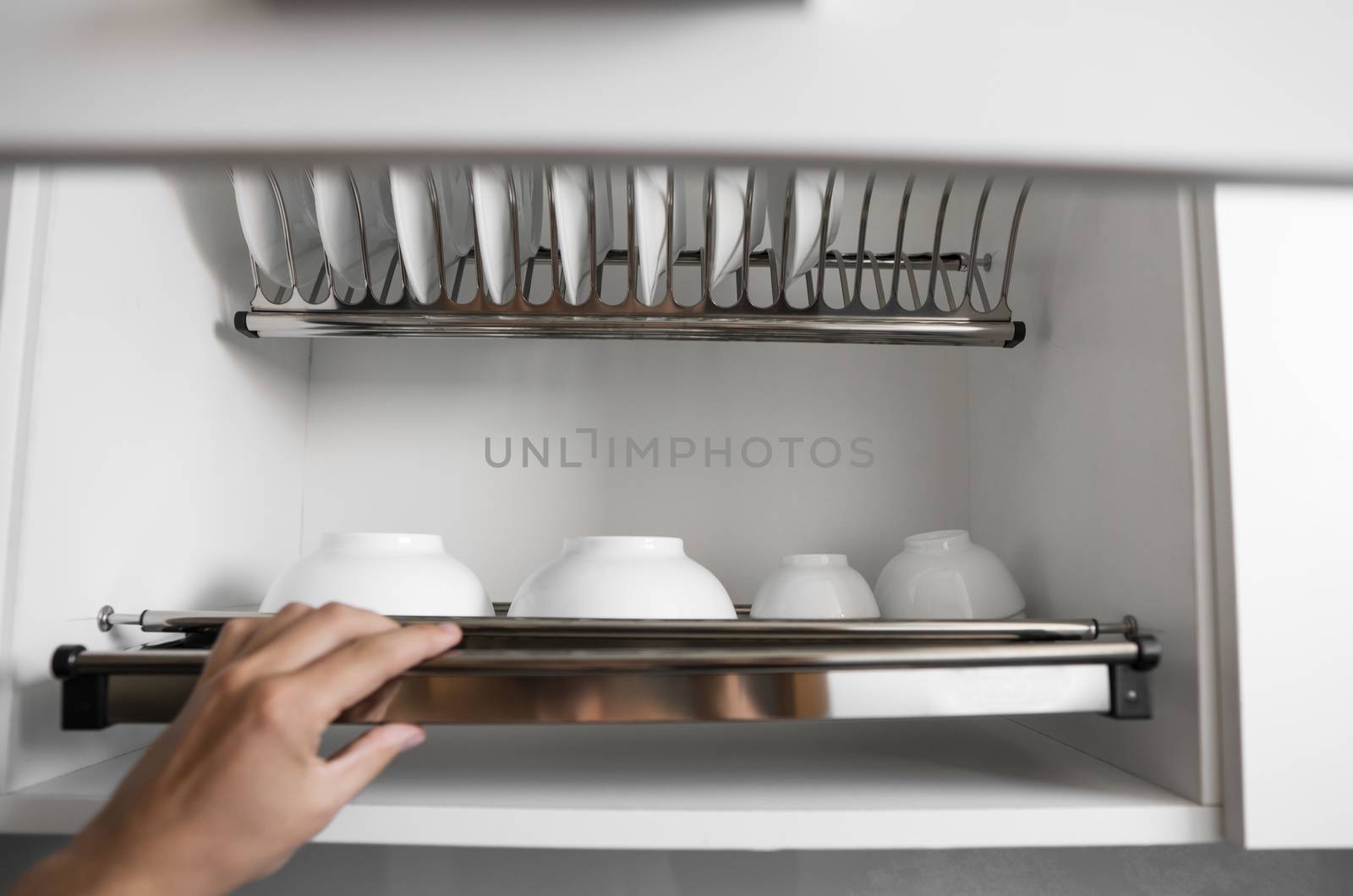 Dish drying metal rack with big nice white clean plates. Traditional comfortable kitchen. Open white dish draining closet with wet dishes of glass and ceramic, plates, bowls drying inside on rack