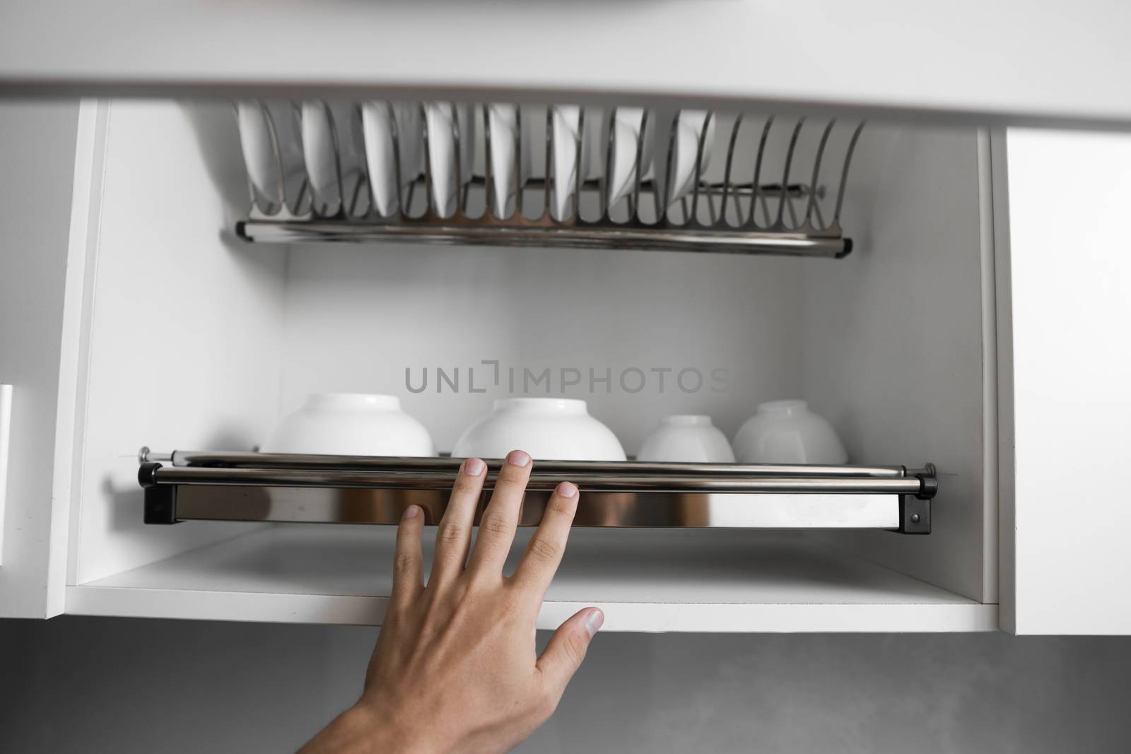 Dish drying metal rack with big nice white clean plates. Traditional comfortable kitchen. Open white dish draining closet with wet dishes of glass and ceramic, plates, bowls drying inside on rack