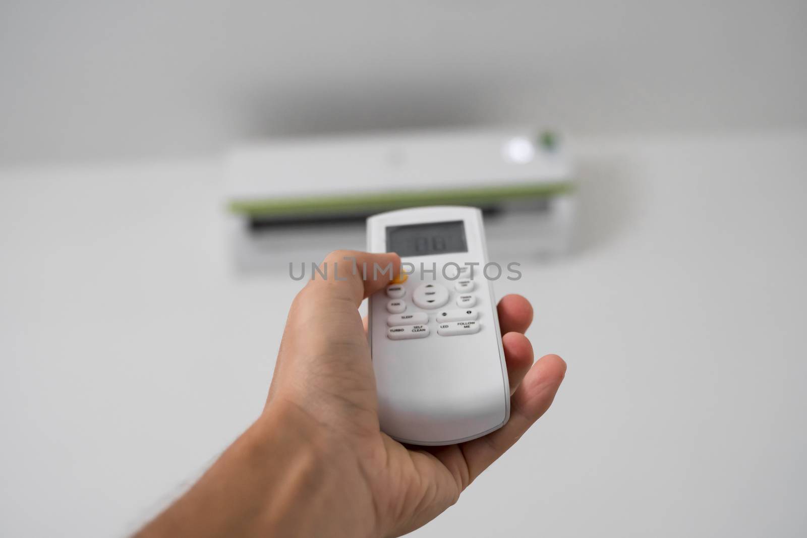 Man's hand using remote controler. Hand holding rc and adjusting temperature of air conditioner mounted on a white wall. Indooor comfort temperature. Health concepts and energy savings. by vovsht