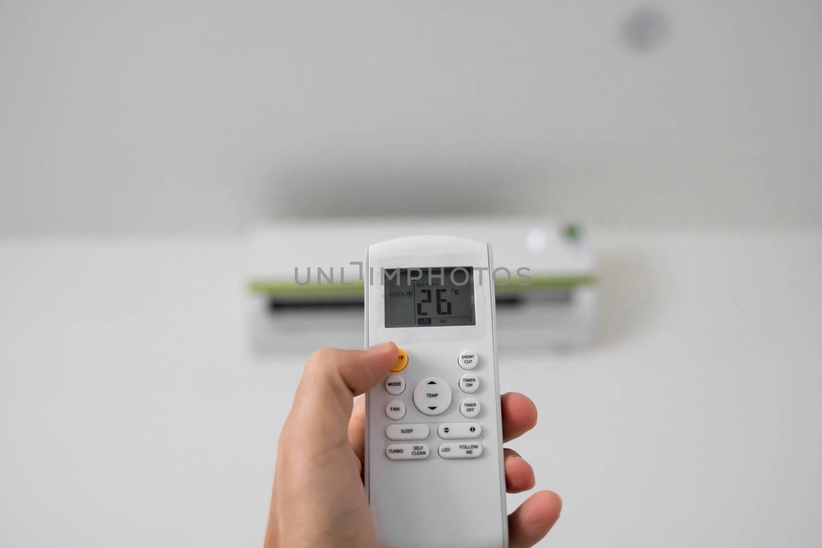 Man's hand using remote controler. Hand holding rc and adjusting temperature of air conditioner mounted on a white wall. Indooor comfort temperature. Health concepts and energy savings