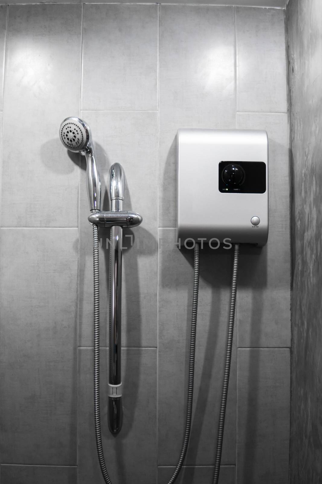 Instant tankless electric water heater installed on grey tile wall with input and output pipe outlet and elcb safety breaker system and silver shower. by vovsht