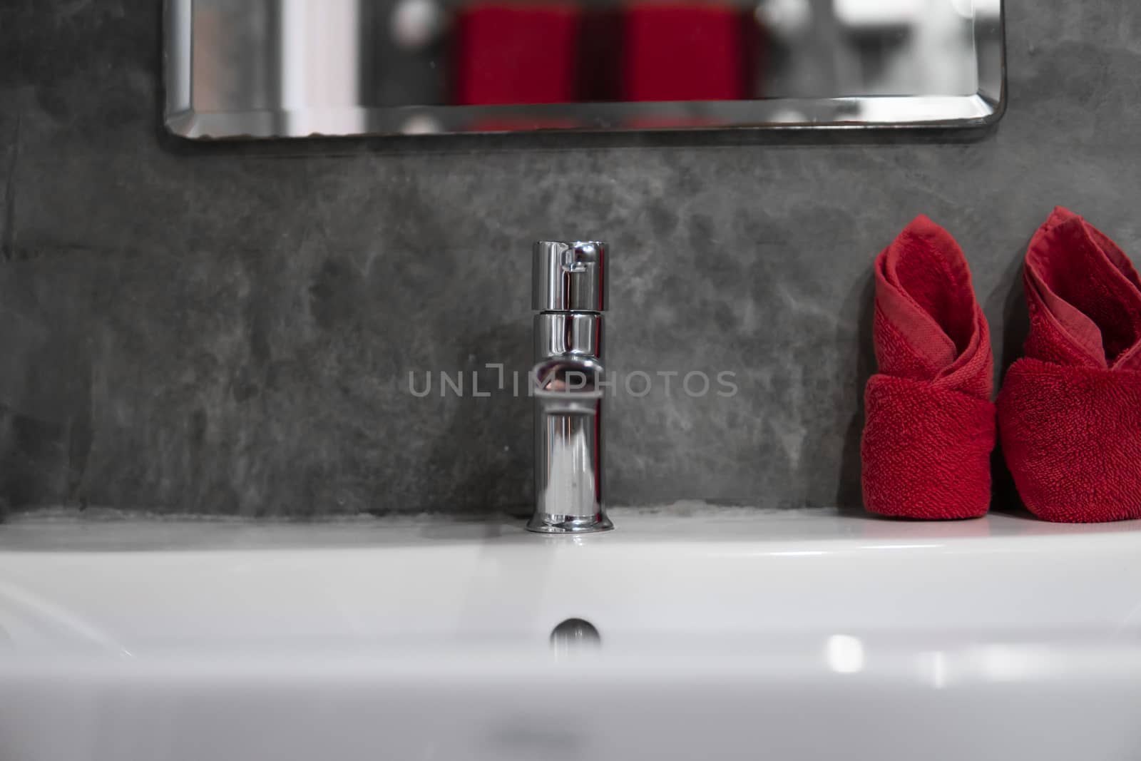 Modern stainless steel faucet with wash basin sink with a two red towels on it . Counter bathroom interior contemporary. Luxury and stylish design bathroom with a concrete style walls