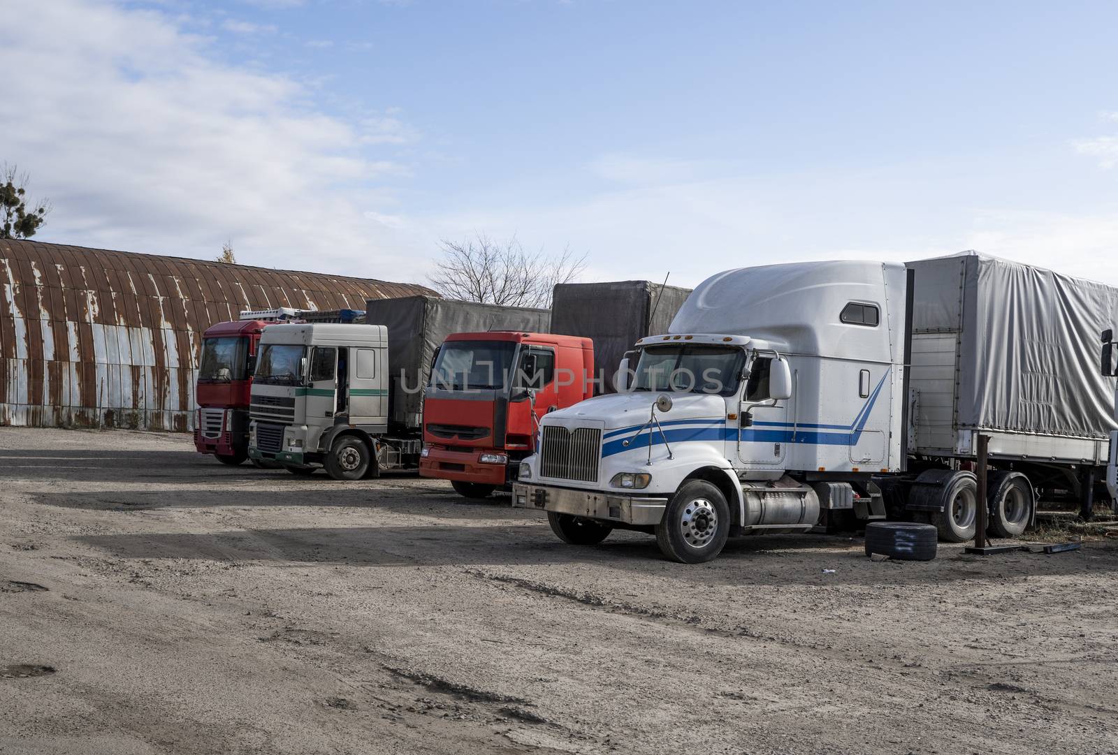 Modern trucks of various colors and models are involved for the transportation of different kinds of commercial goods are in a row on truck stop in anticipation of the continuation of working flights. by vovsht