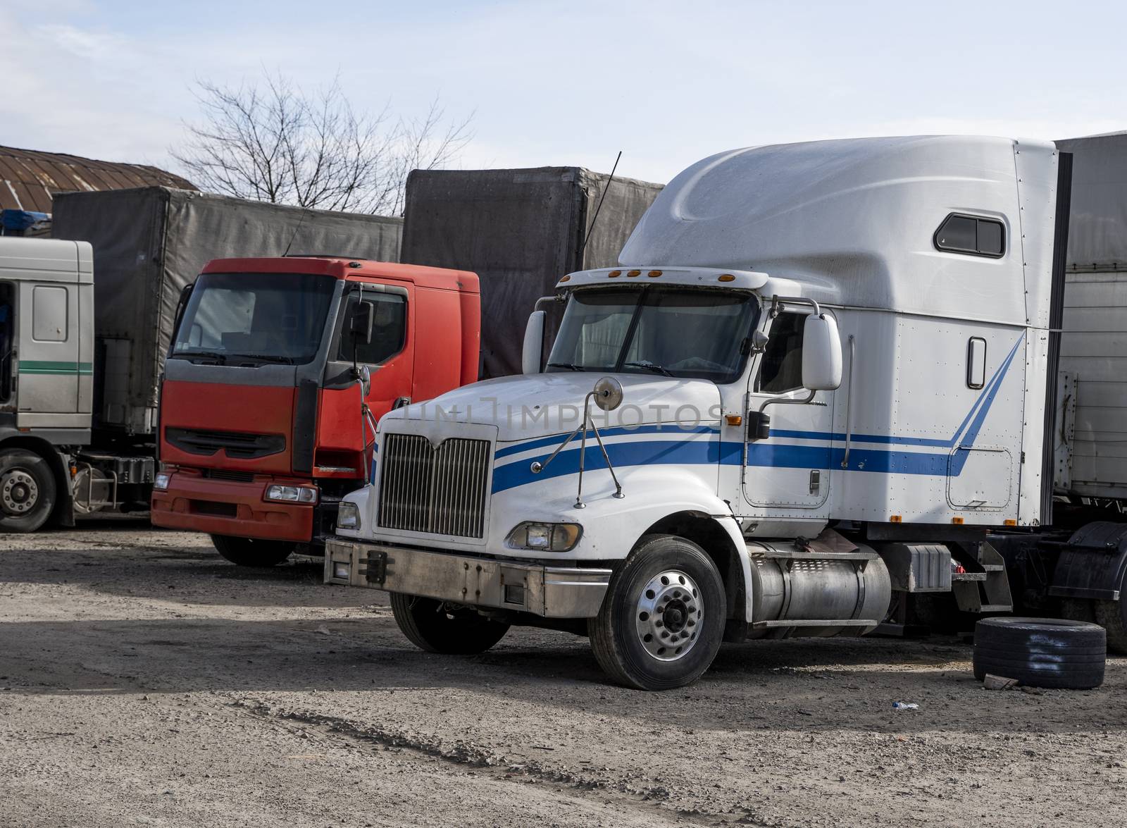 Modern trucks of various colors and models are involved for the transportation of different kinds of commercial goods are in a row on truck stop in anticipation of the continuation of working flights. by vovsht