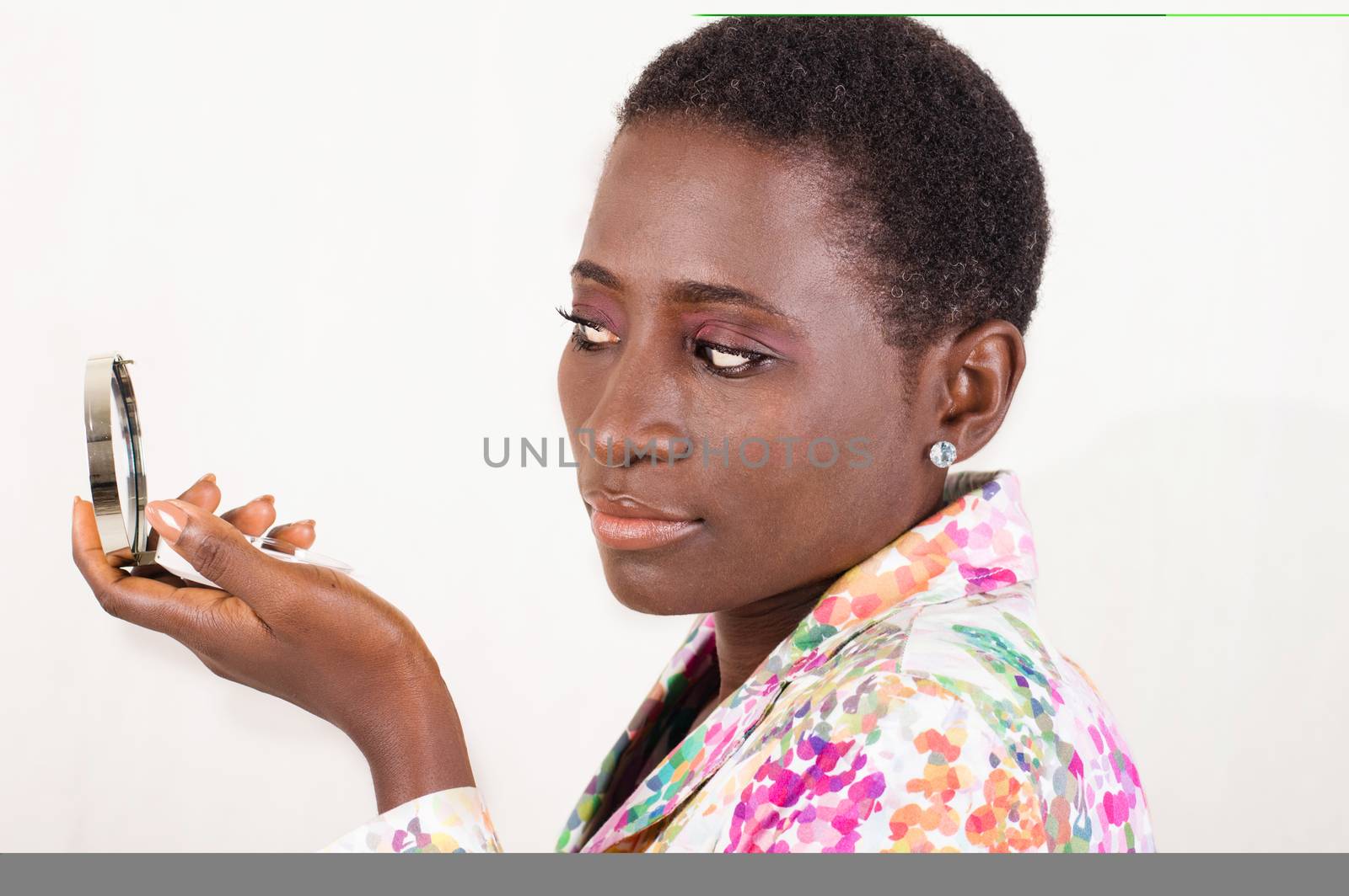 Young African woman looks at the small mirror to see the beauty of her makeup.