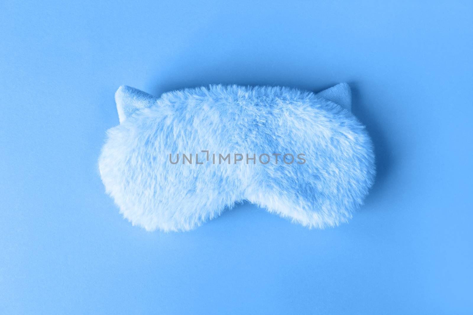 Fluffy fur sleep mask with small ears on paper background. Top view, flatlay. Accessories for girls and young women in Classic Blue colour, close-up, top view. Color of the year 2020 concept.