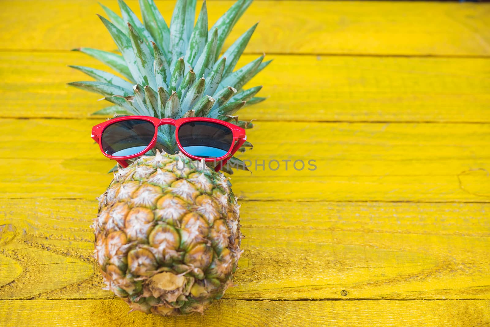 Holiday pineapple have sunglasses on yellow  wooden background, tropical holiday concept
