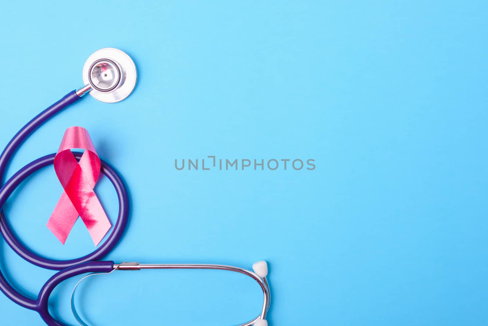 Breast cancer month concept, flat lay top view, pink ribbon and stethoscope on blue background with copy space for your text
