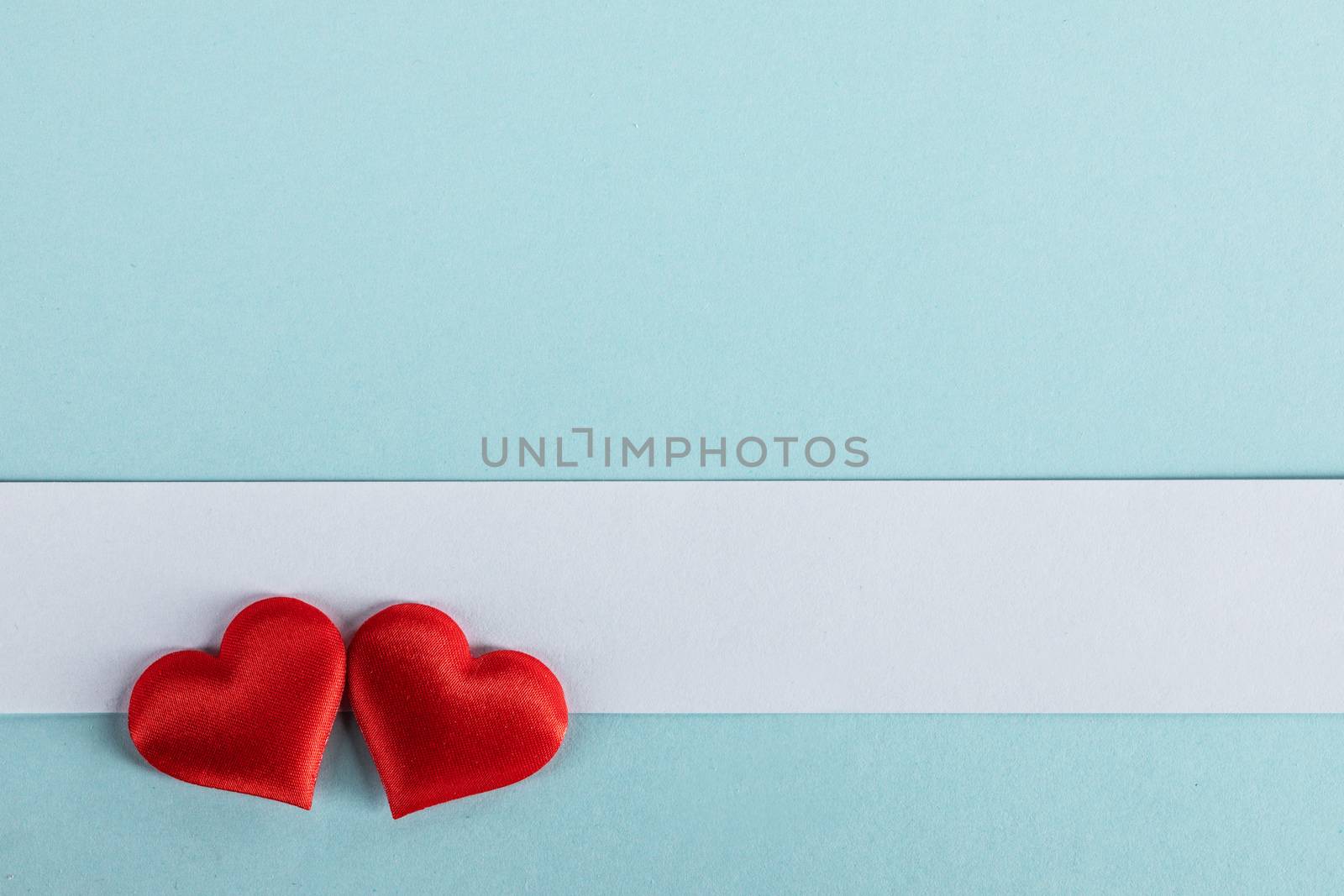Valentine's day two red silk hearts and white paper on blue paper background, love concept