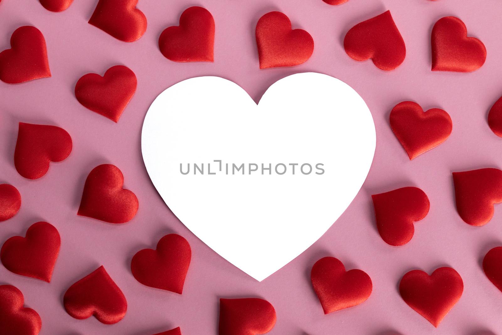 Valentine's day many red silk hearts and white heart shaped card on pink background, love concept