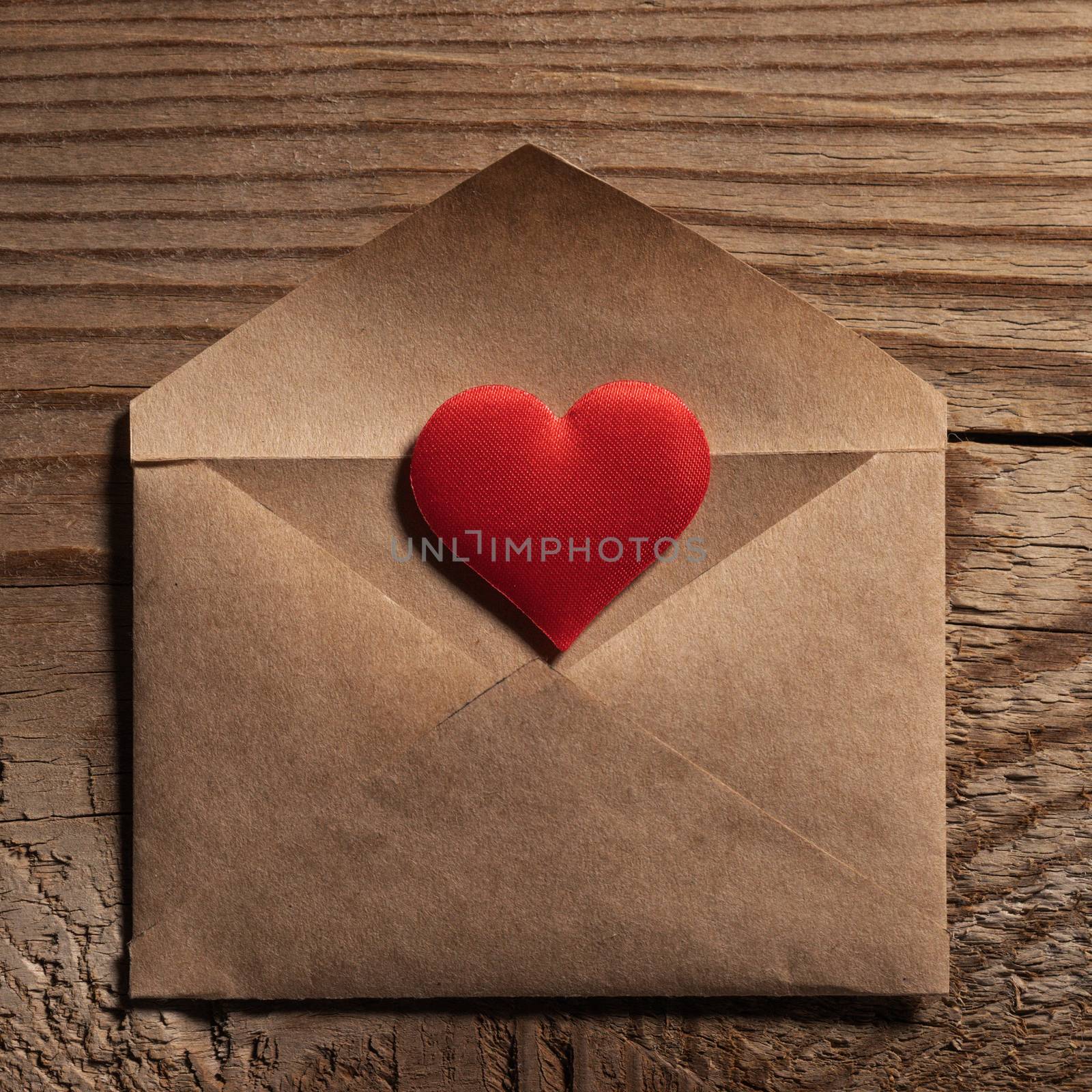 Valentine day love letter, envelope of craft paper with red heart on wooden background