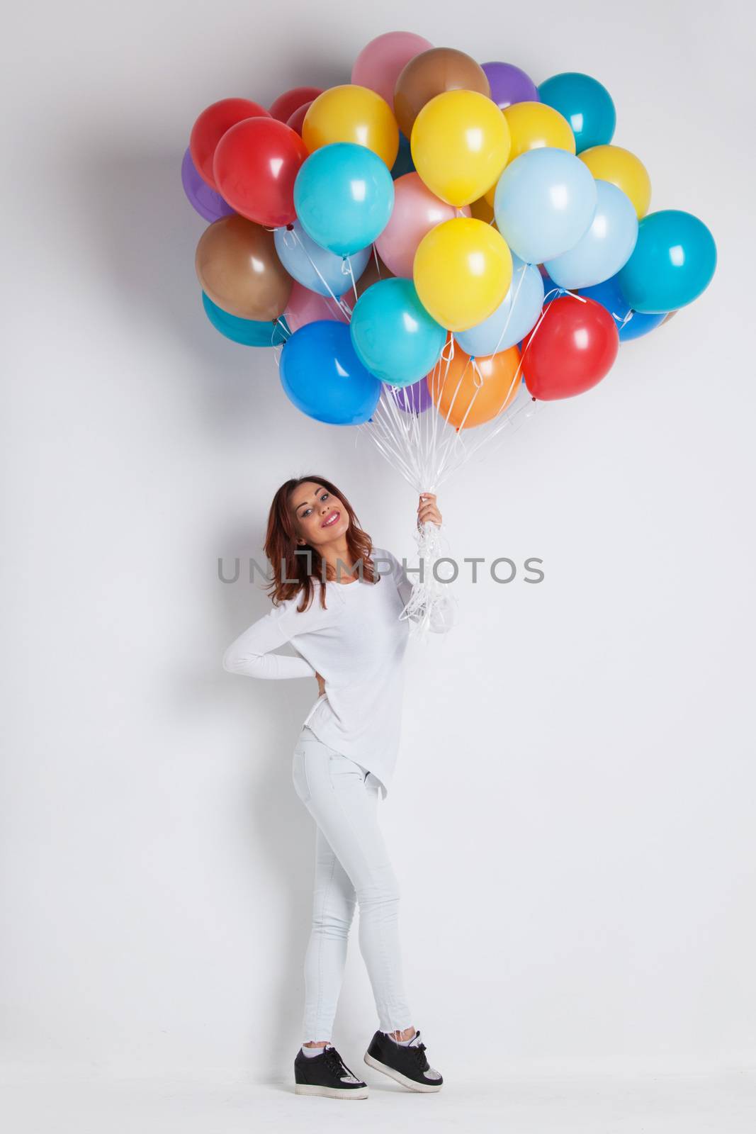 Young pretty woman in white clothes with colored balloons on white background with copy space for text