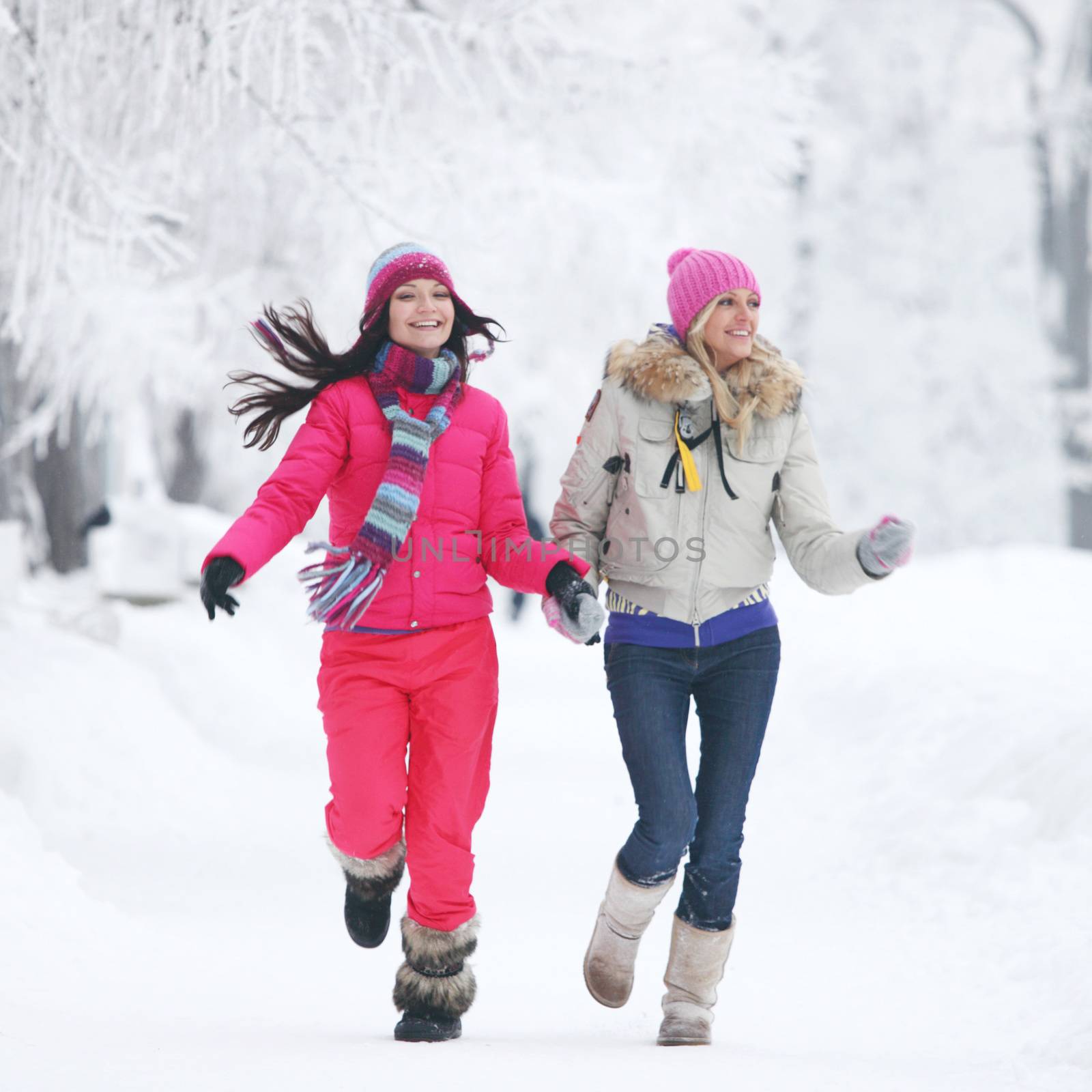 Two young happy smiling women running in the winter park