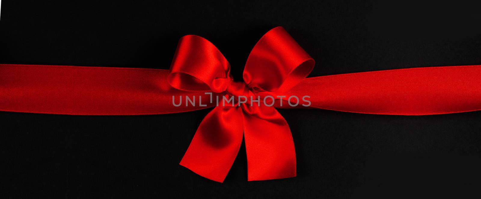 Red satin ribbon bow on black paper background