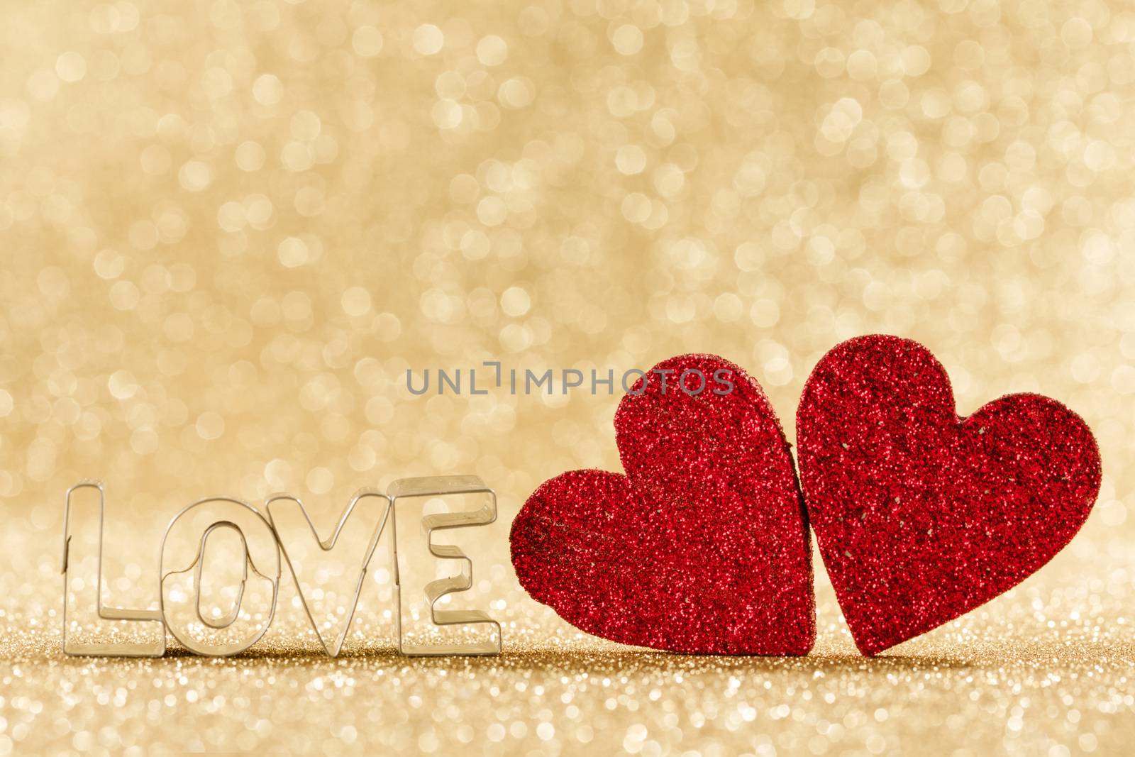 Two red handmade glitter hearts and word love on golden bright glitter lights bokeh background