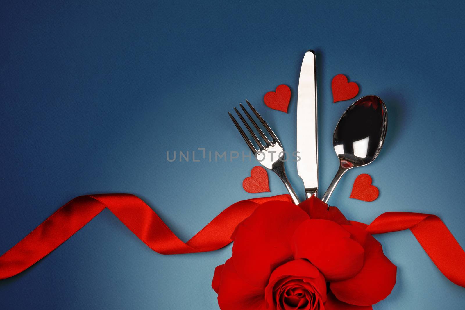 Cutlery set tied with silk ribbon rose flower and hearts on blue background Valentine day romantic dinner concept