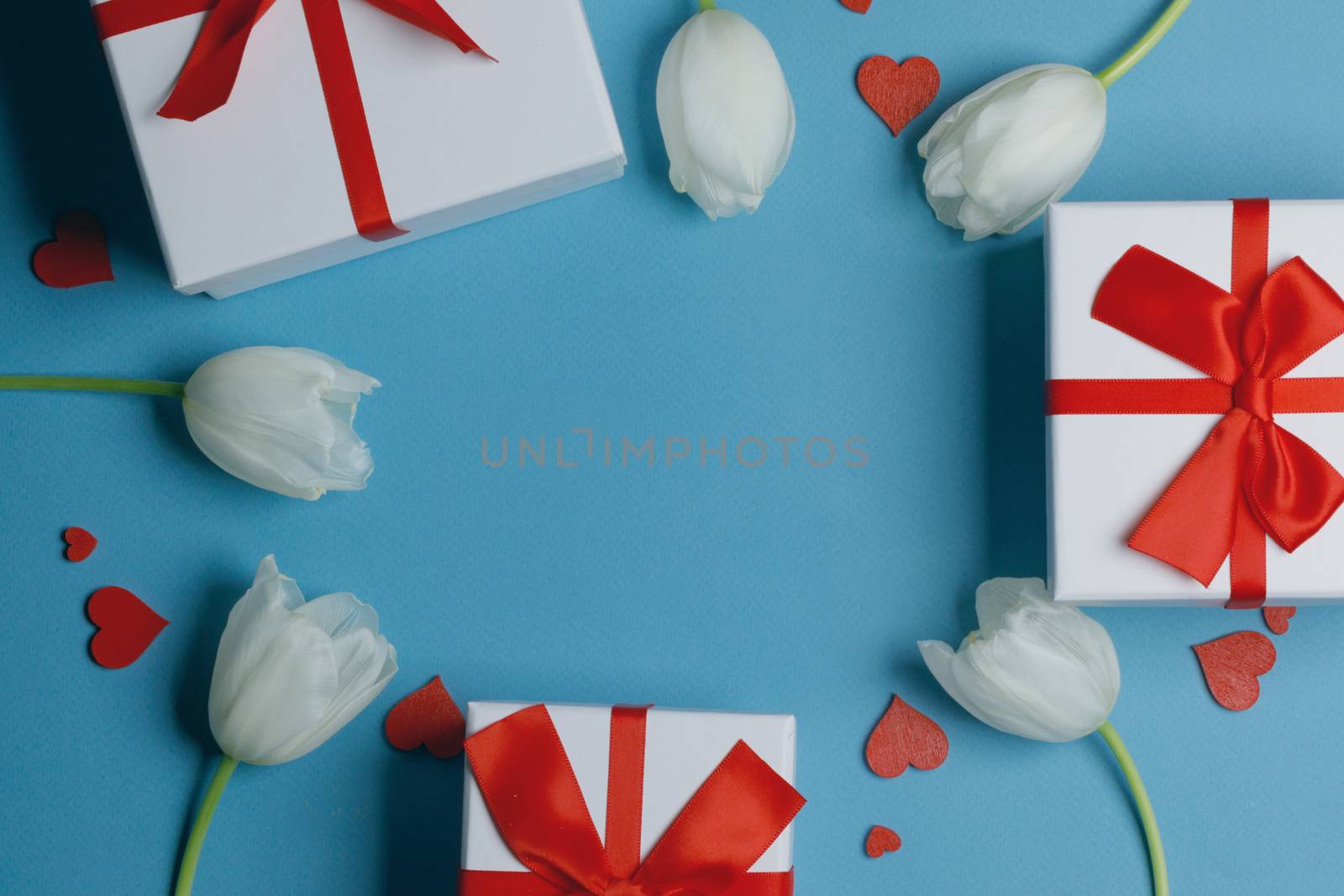 White tulip flowers gifts red hearts and gifts composition on blue background top view with copy space. Valentine's day, birthday, wedding, Mother's day concept. Copy space